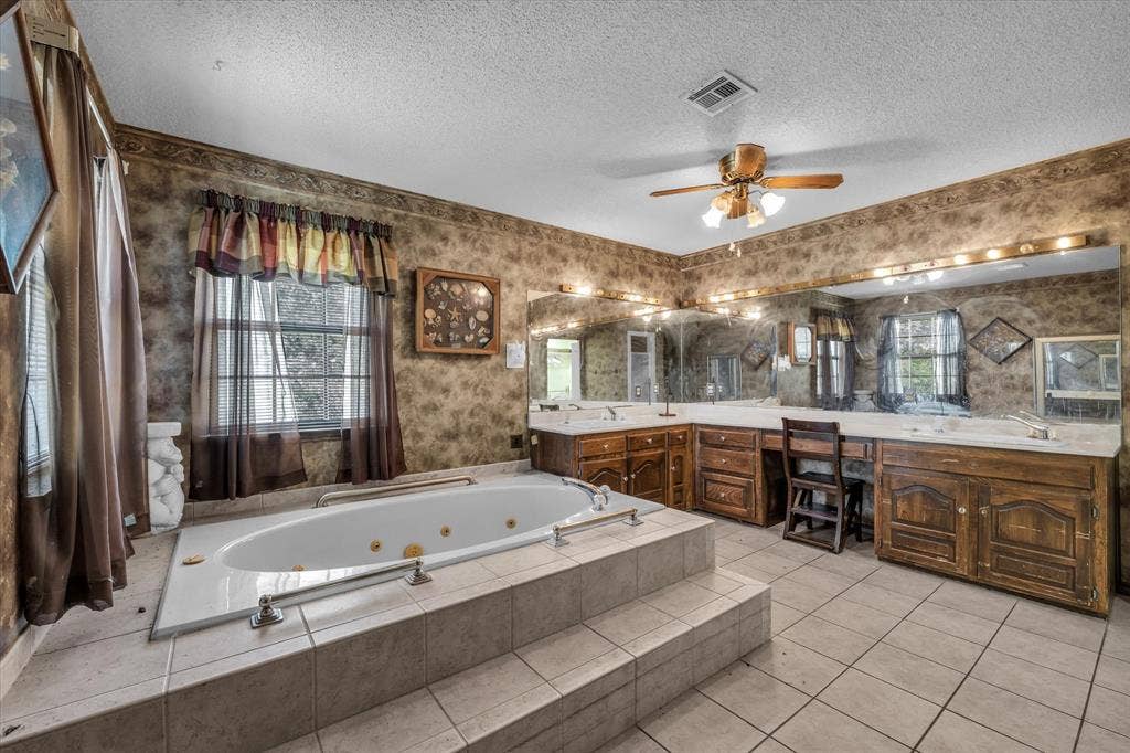 4201 N 19th Street, Waco, TX 76708 Built-in jetted tub with tiled surround, dual vanity with wood cabinetry, large vanity mirror with integrated lighting, and ceiling fan