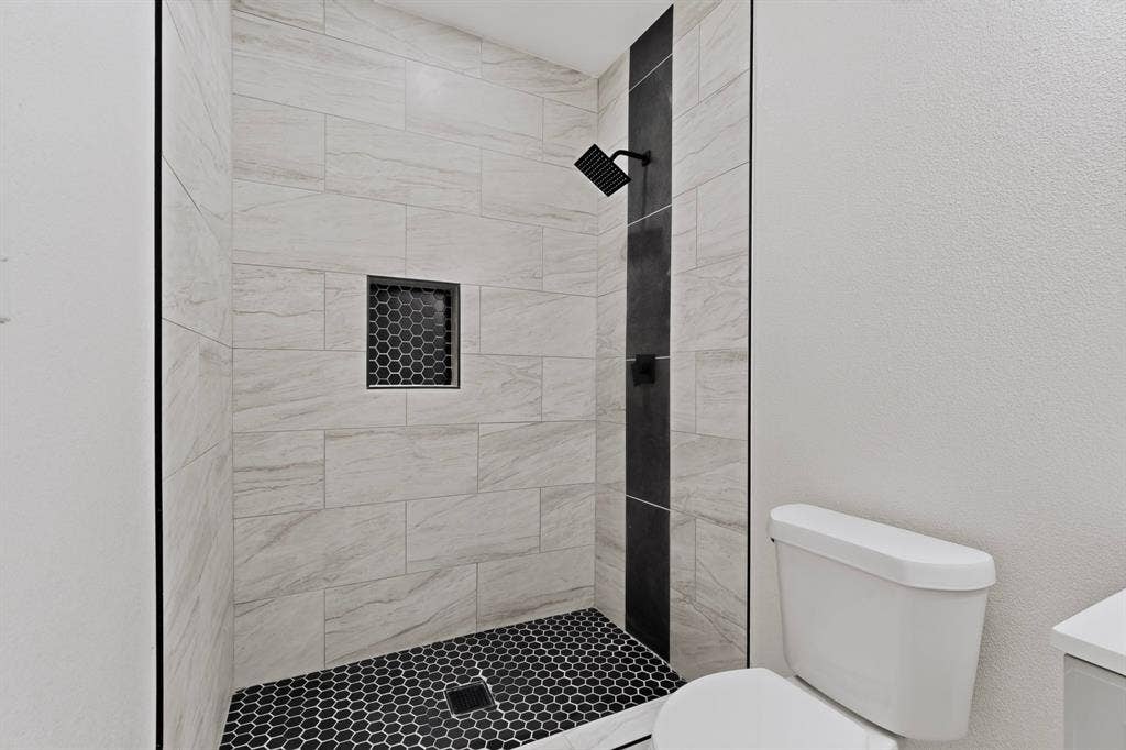 651 Ezekial Avenue, Dallas, TX 75217 Shower with large format wall tiling, black accent tile, black hexagon tile flooring, and a matte black shower head