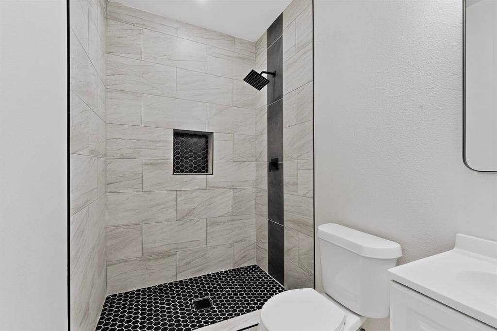 651 Ezekial Avenue, Dallas, TX 75217 Shower enclosure featuring large format light-toned tile, a black hexagon tile floor, and a recessed shower niche