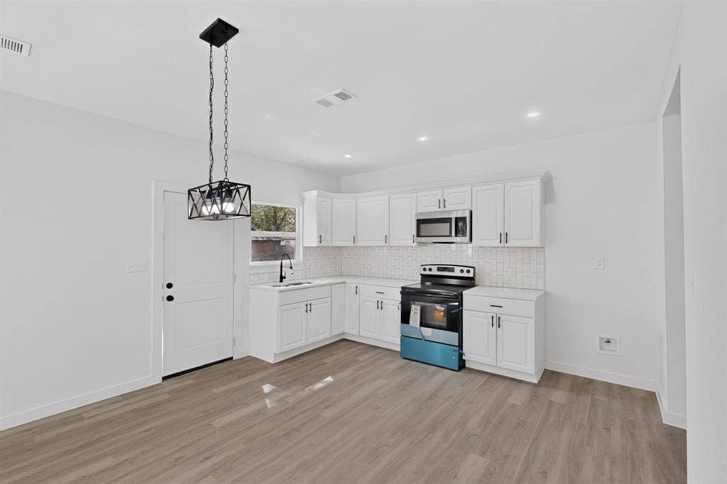 651 Ezekial Avenue, Dallas, TX 75217 Kitchen featuring white shaker-style cabinetry, a subway tile backsplash, stainless steel microwave, black electric range, and wood-finish flooring