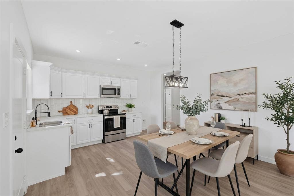 651 Ezekial Avenue, Dallas, TX 75217 White shaker cabinetry with dark hardware, stainless steel appliances, light wood-finish flooring, recessed lighting, and a linear chandelier