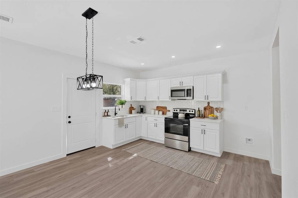 651 Ezekial Avenue, Dallas, TX 75217 Contemporary kitchen featuring white cabinetry, stainless steel appliances, light-toned wood-finish flooring, and a decorative pendant light fixture