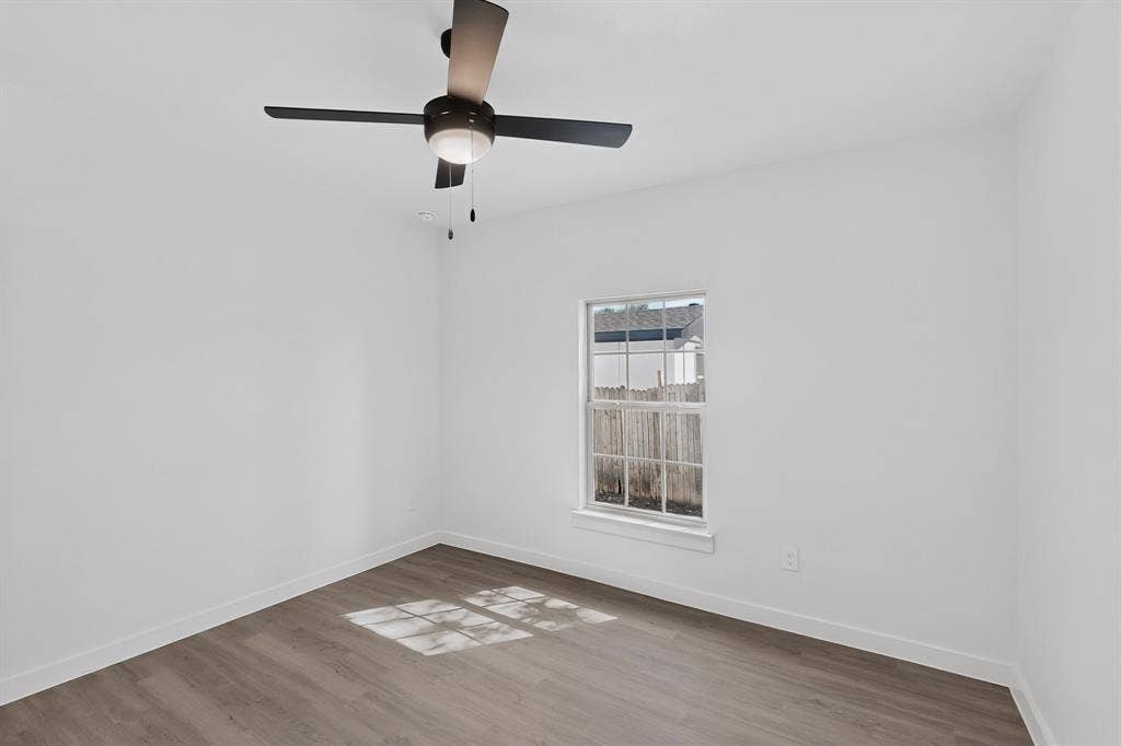 651 Ezekial Avenue, Dallas, TX 75217 Neutral white wall paint, a window with a white frame, wood-finish flooring, and a ceiling fan with integrated lighting