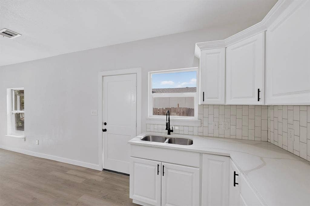 651 Ezekial Avenue, Dallas, TX 75217 White shaker cabinetry, light-toned wood-finish flooring, white subway tile backsplash, and a double basin stainless steel sink