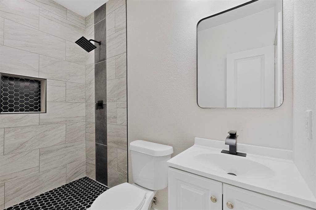 651 Ezekial Avenue, Dallas, TX 75217 Shower with contrasting tile accents, black hexagonal floor tiles, and a recessed niche