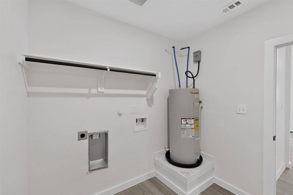 651 Ezekial Avenue, Dallas, TX 75217 Laundry area with water heater on a raised platform, white walls, wood-finish flooring, and a built-in shelf with hanging rod