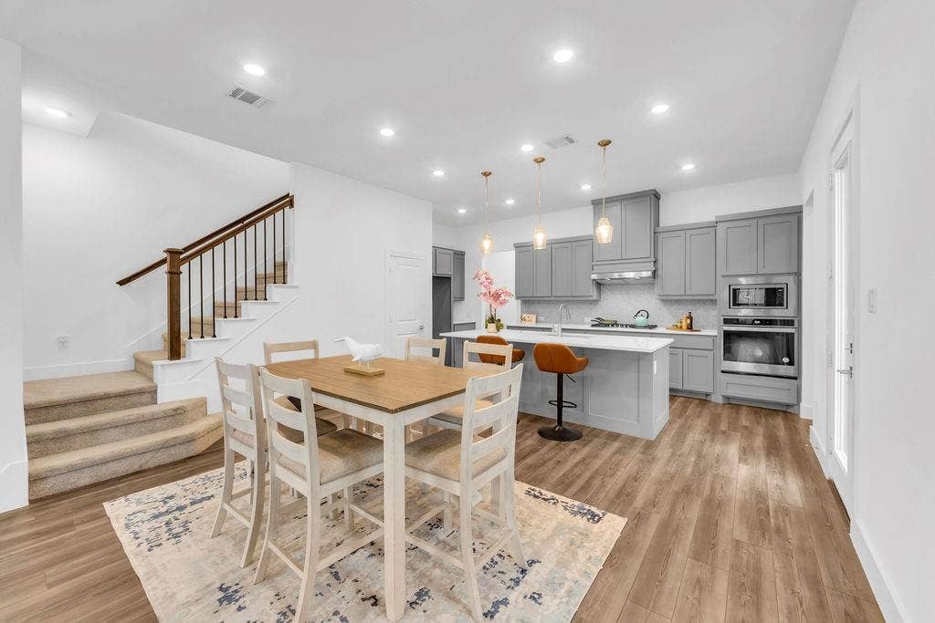 8300 Bethpage Drive, McKinney, TX 75070 Open-concept layout featuring wood-finish flooring, a kitchen with gray cabinetry, stainless steel appliances, a white island with seating, and recessed lighting