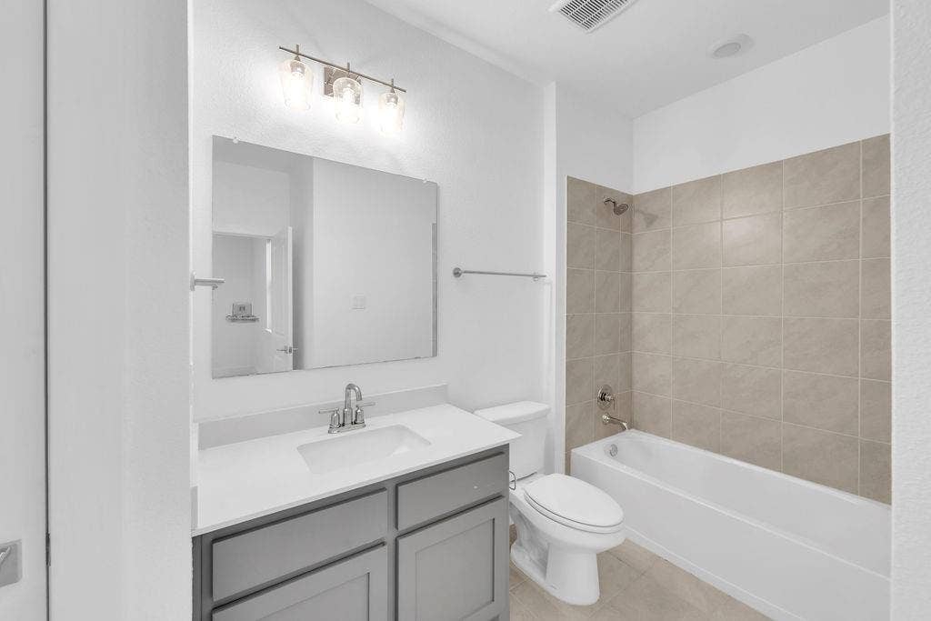 8300 Bethpage Drive, McKinney, TX 75070 Vanity with gray cabinetry and white countertop, undermount sink with chrome faucet, framed mirror, and three-light fixture