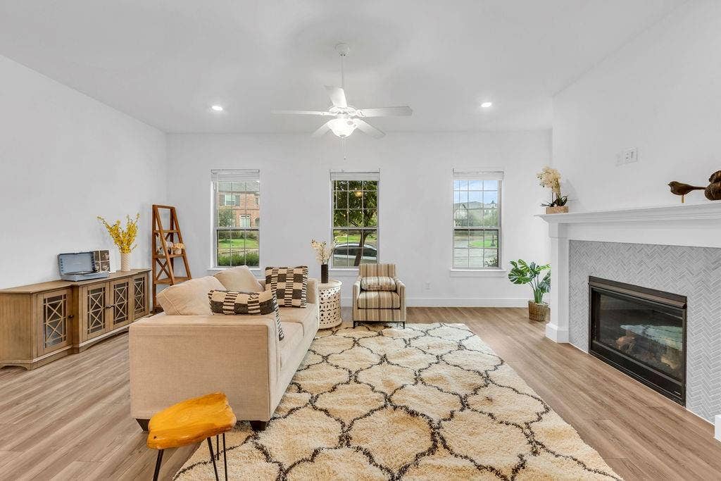8300 Bethpage Drive, McKinney, TX 75070 Recessed lighting, wood-finish flooring, white ceiling fan, multiple windows, and a built-in fireplace with a tile surround and mantel