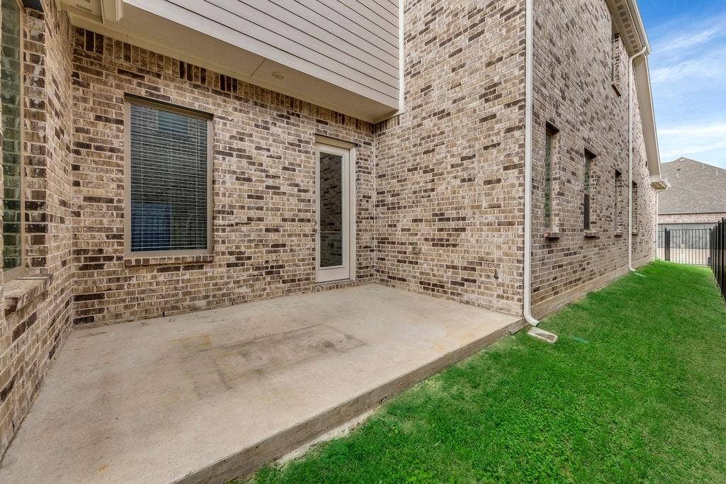 8300 Bethpage Drive, McKinney, TX 75070 Concrete patio with a brick exterior, single-pane door, and multiple windows with blinds