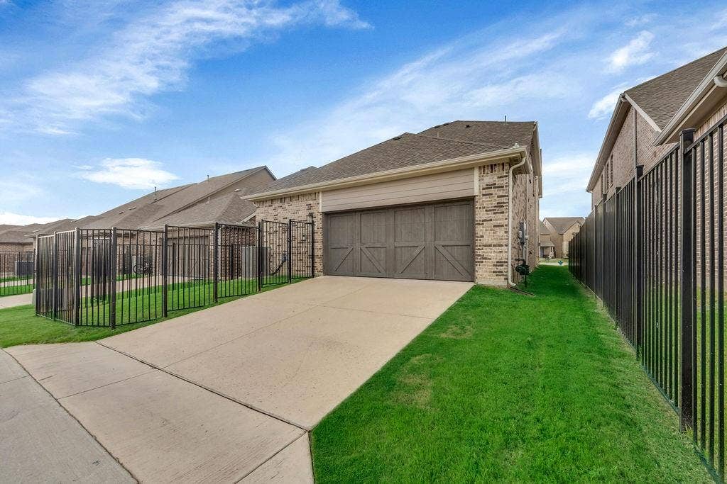 8300 Bethpage Drive, McKinney, TX 75070 Concrete driveway with a wood-finish garage door, brick exterior, and a black metal fence enclosing a grass lawn