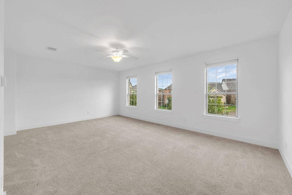 8300 Bethpage Drive, McKinney, TX 75070 Expansive room featuring three windows, a ceiling fan with integrated lighting, and neutral-toned carpeting