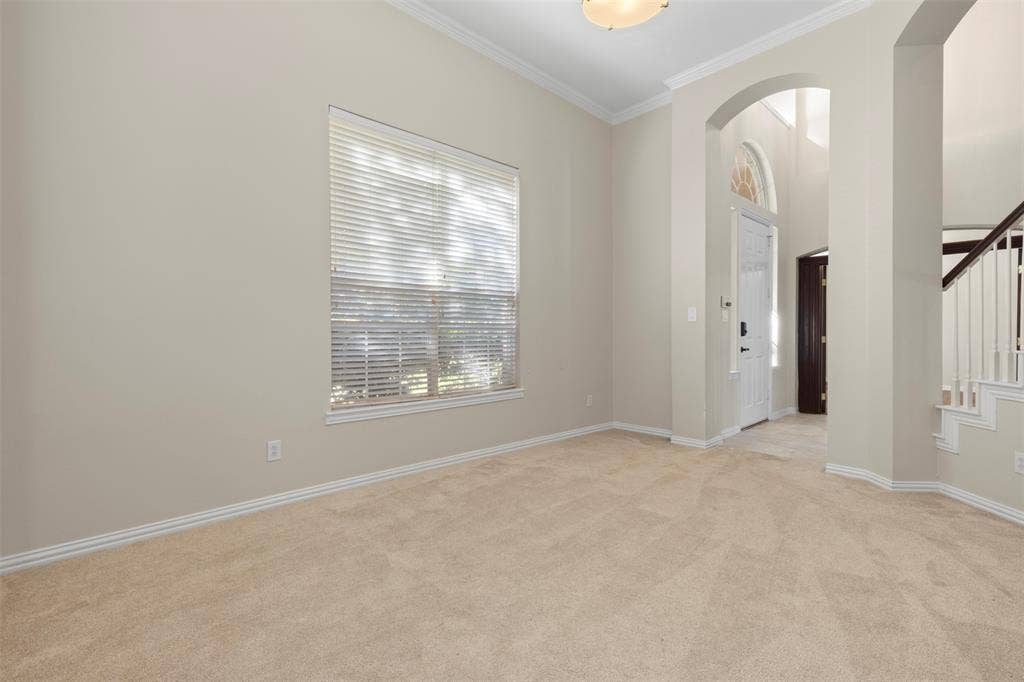 5401 Wolcott Place, Richardson, TX 75082 Neutral tone wall paint, crown molding, arched entryways, natural light from a large window, and light-colored carpeting