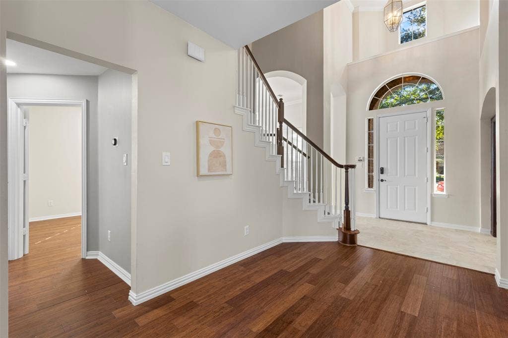 5401 Wolcott Place, Richardson, TX 75082 Two-story foyer with wood-finish flooring, a grand staircase with white risers and dark wood handrail, an arched entry door with transom window, and a high ceiling with an overhead light fixture