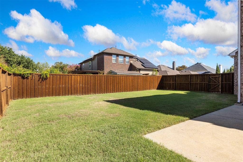 5401 Wolcott Place, Richardson, TX 75082 Expansive grassy backyard featuring a perimeter wood fence, concrete patio, and a wood gate