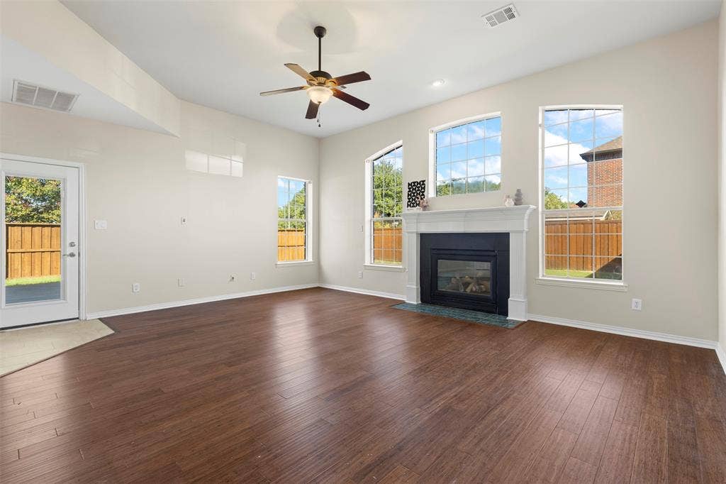 5401 Wolcott Place, Richardson, TX 75082 Spacious interior with wood-finish flooring, a fireplace with a white mantel, and multiple large grid-pattern windows