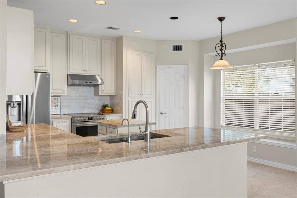 5401 Wolcott Place, Richardson, TX 75082 Spacious kitchen featuring an expansive island with a double basin sink, light-toned cabinetry, stainless steel range with overhead hood, and recessed lighting
