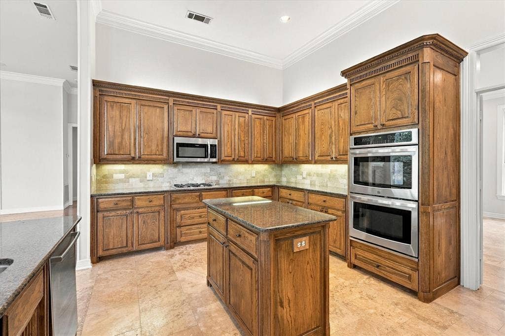 Full kitchen featuring wood cabinetry, stainless steel appliances, a center island with countertop, tile flooring, and crown molding