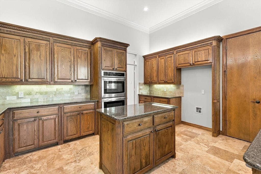Kitchen with wood-finish cabinetry, granite countertops, tile backsplash, stainless steel double oven, and a central island with storage