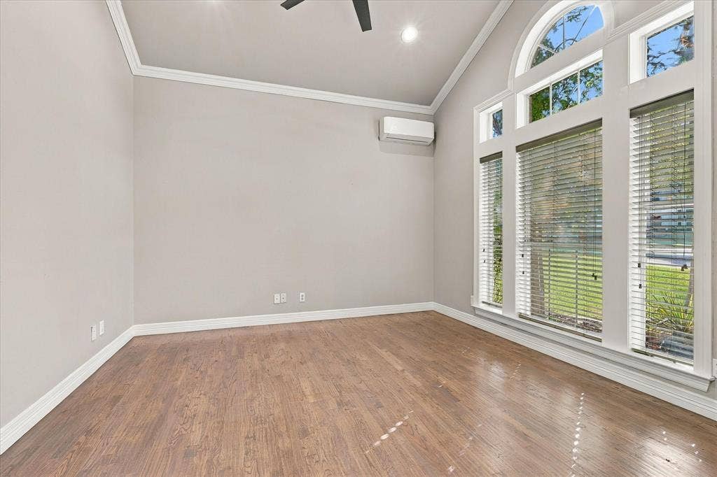 Vaulted ceiling, wood-finish flooring, architectural windows with an arched transom, crisp white trim, and a wall-mounted mini-split system