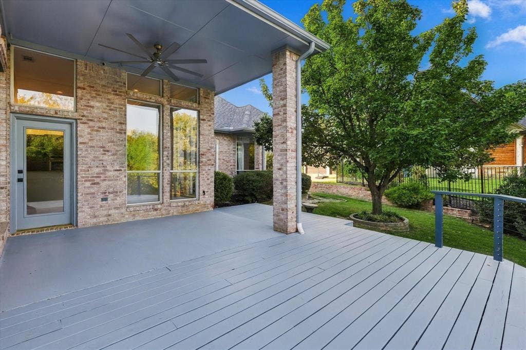 Expansive outdoor deck featuring a covered patio, ceiling fan, brick exterior, and a manicured lawn