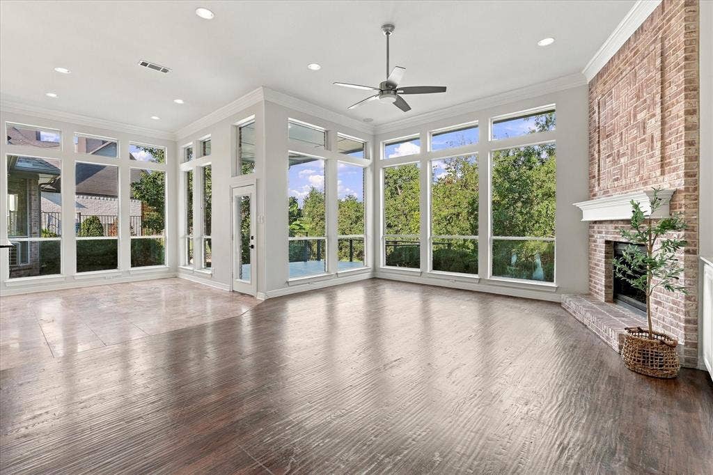 Expansive room featuring multi-pane windows, a brick-surround fireplace with a white mantel, and wood-finish flooring