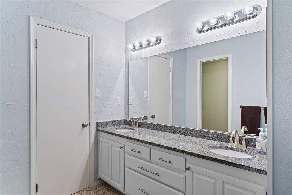 Double vanity with integrated sinks, granite countertop, chrome fixtures, white cabinetry, and vanity lighting