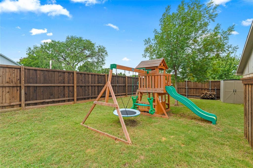 Fenced backyard with a grassy lawn, mature trees, and an outdoor storage shed