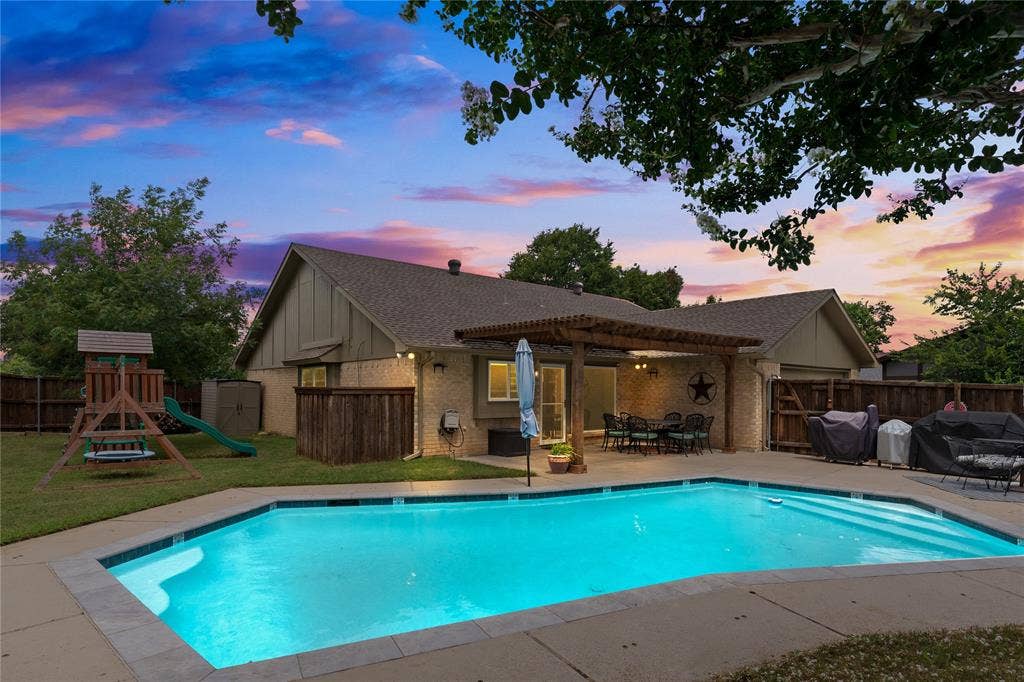 Expansive backyard featuring a built-in swimming pool with decking, a covered patio with a wood pergola, and a grassy area for pets or play!