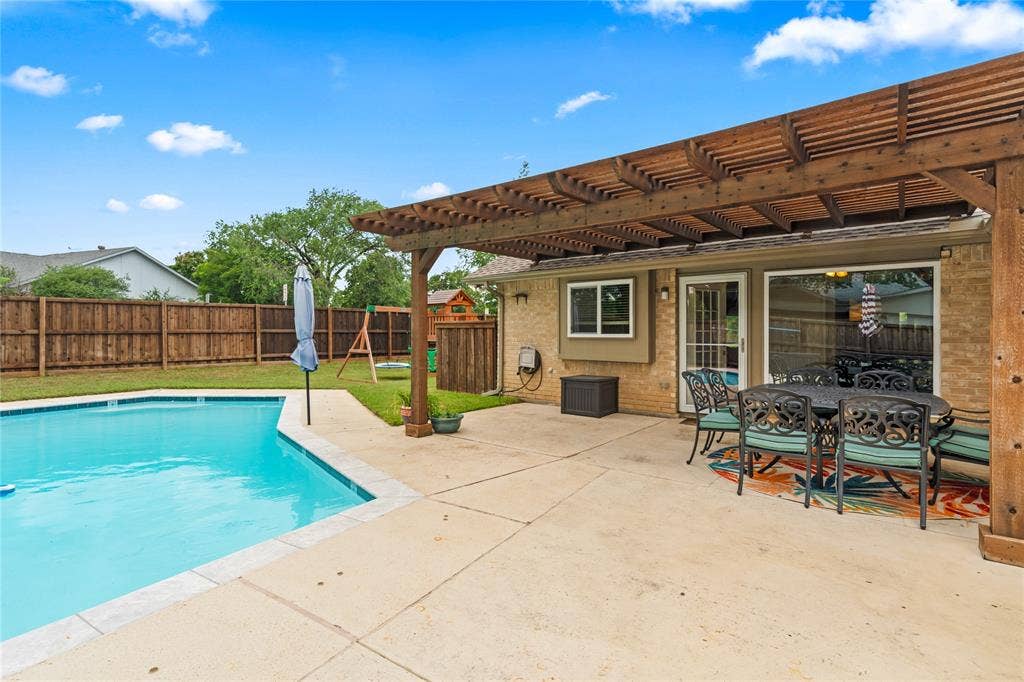 Expansive patio and decking with a wooden pergola, swimming pool, and wood privacy fencing