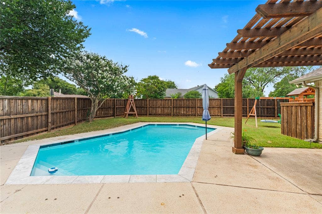Backyard featuring a built-in swimming pool with concrete decking, a wooden pergola, and perimeter wood fencing
