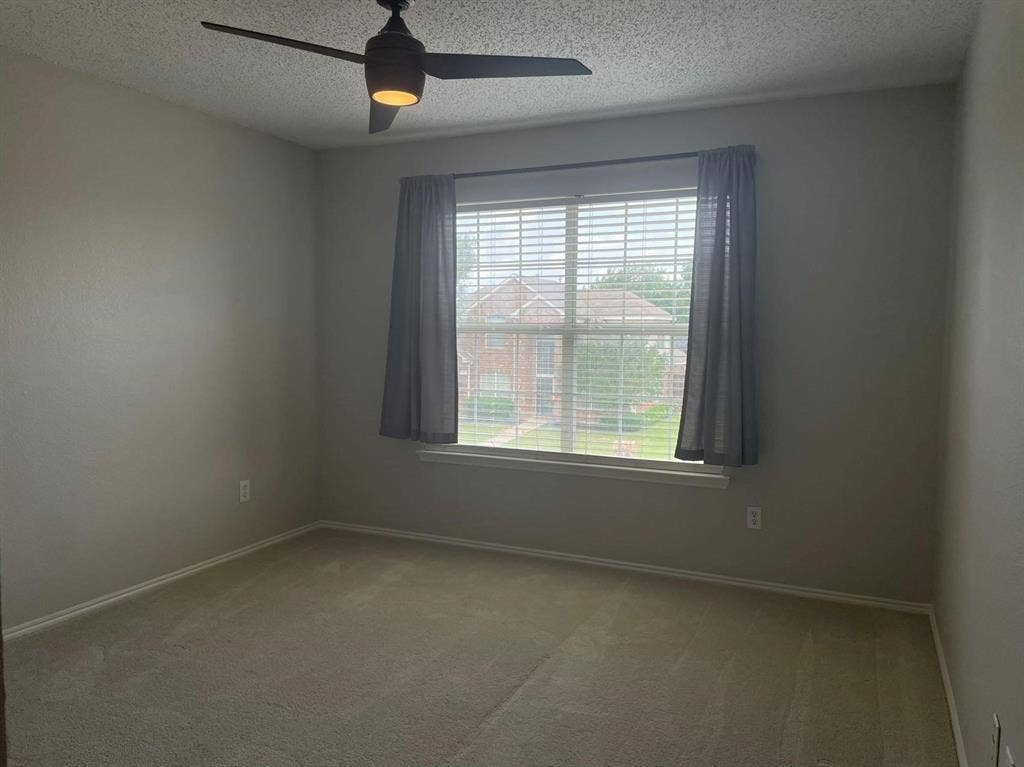 Neutral-toned walls, plush wall-to-wall carpeting, large window with integrated blinds, and a modern ceiling fan with light fixture