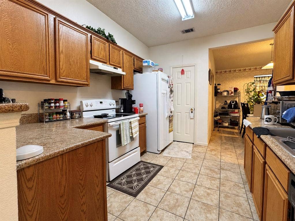 725 Andalusia Trail, DeSoto, TX 75115 Kitchen featuring ample wood cabinetry, speckled countertops, a white electric range, a white refrigerator, and tile flooring