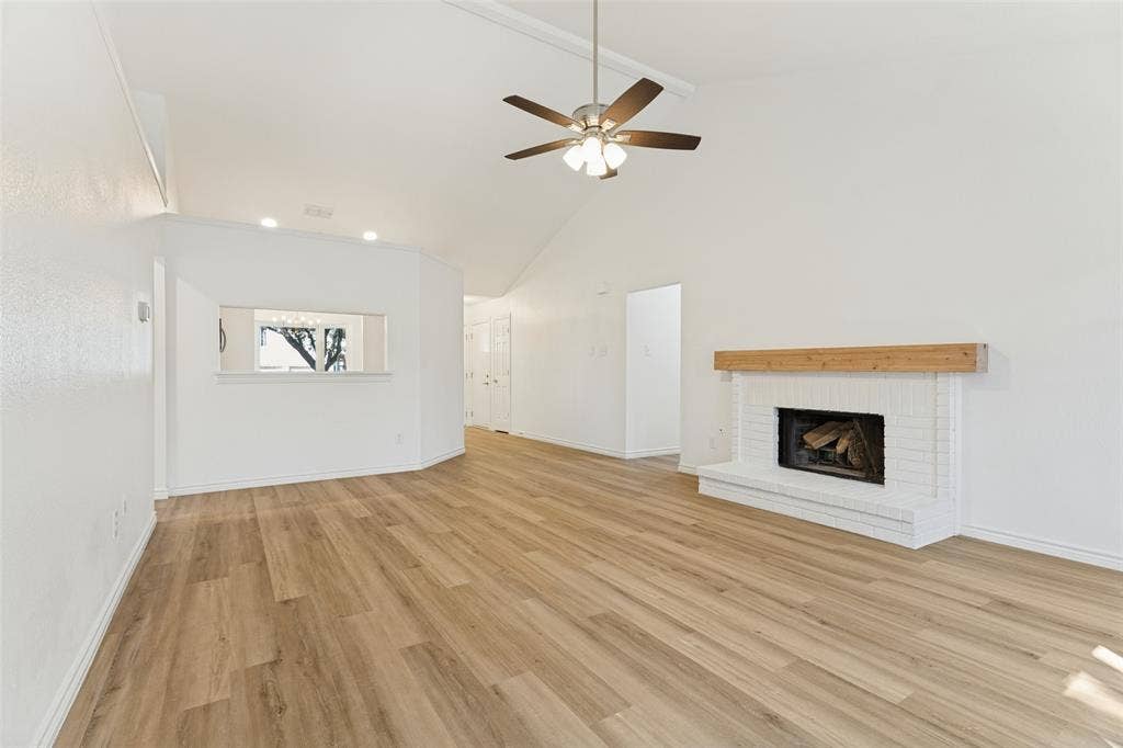 7440 Bear Lake Drive, Fort Worth, TX 76137 Vaulted ceiling with a ceiling fan, wood-finish flooring, white brick fireplace with a wood mantle, and an interior pass-through window