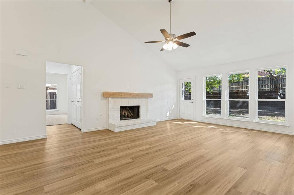 7440 Bear Lake Drive, Fort Worth, TX 76137 Vaulted ceiling, wood-finish flooring, white brick fireplace with wood mantel, ceiling fan, and multiple large windows