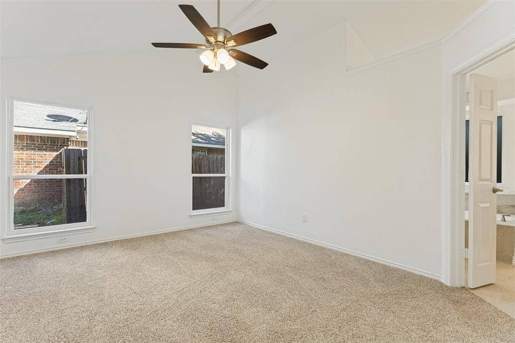 7440 Bear Lake Drive, Fort Worth, TX 76137 Carpeted room featuring a vaulted ceiling with a ceiling fan, two windows, and direct access to a tiled bathroom