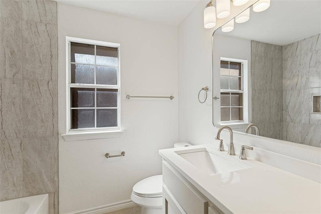 7440 Bear Lake Drive, Fort Worth, TX 76137 White vanity with integrated sink, brushed nickel faucet, large wall mirror, and modern lighting fixture