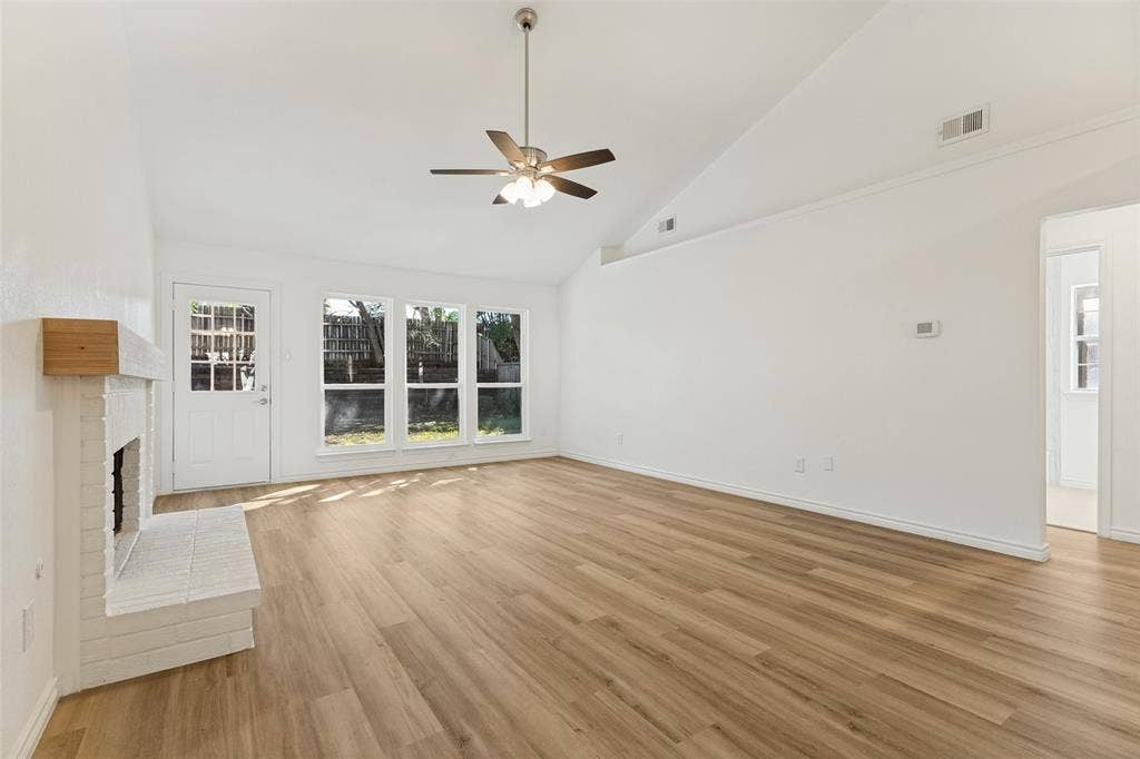 7440 Bear Lake Drive, Fort Worth, TX 76137 Vaulted ceiling with ceiling fan, wood-finish flooring, white brick fireplace with wood mantel, multiple windows, and a glass-paneled exterior door