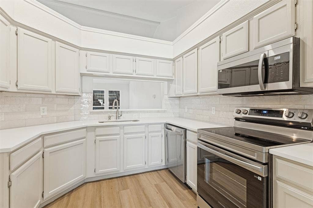 7440 Bear Lake Drive, Fort Worth, TX 76137 White cabinetry, stainless steel appliances, light-toned backsplash, light-toned countertops, and wood-finish flooring