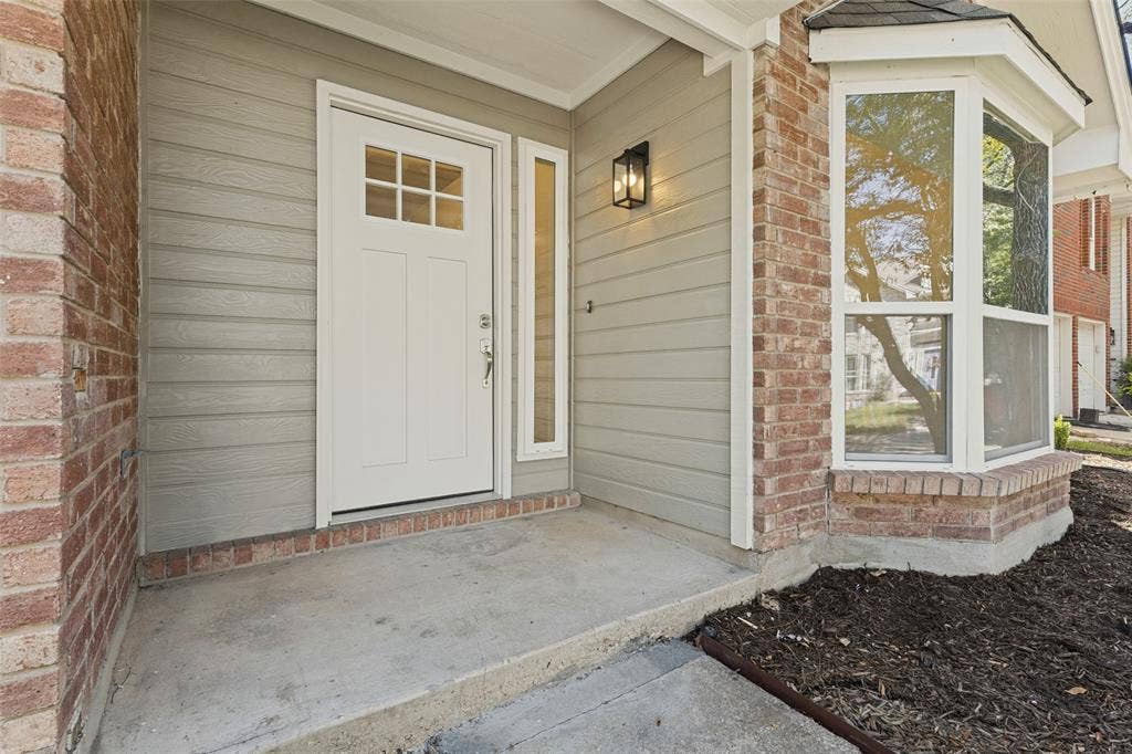 7440 Bear Lake Drive, Fort Worth, TX 76137 Brick and siding exterior with a paneled entry door, transom sidelight, and an exterior wall lantern