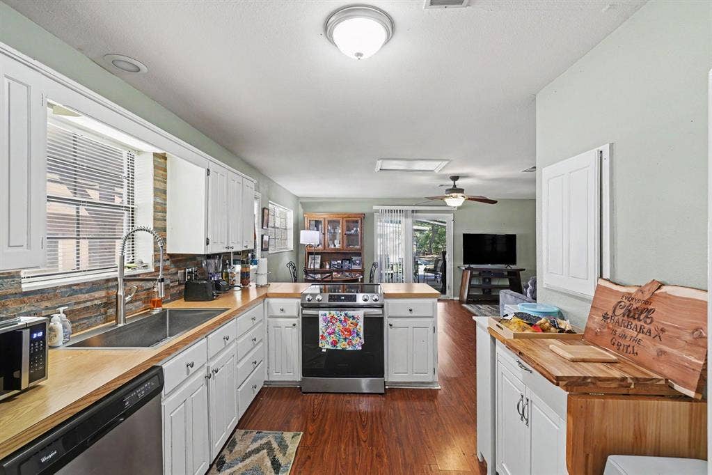 26 Brookhaven Drive, Lucas, TX 75002 White cabinetry with modern hardware, wood-finish countertops, stainless steel sink, and stacked stone-finish backsplash