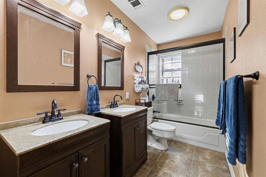 26 Brookhaven Drive, Lucas, TX 75002 Dual vanity with granite-style countertops and undermount sinks, bronze-finish fixtures, and a shower-tub combination with a sliding glass enclosure
