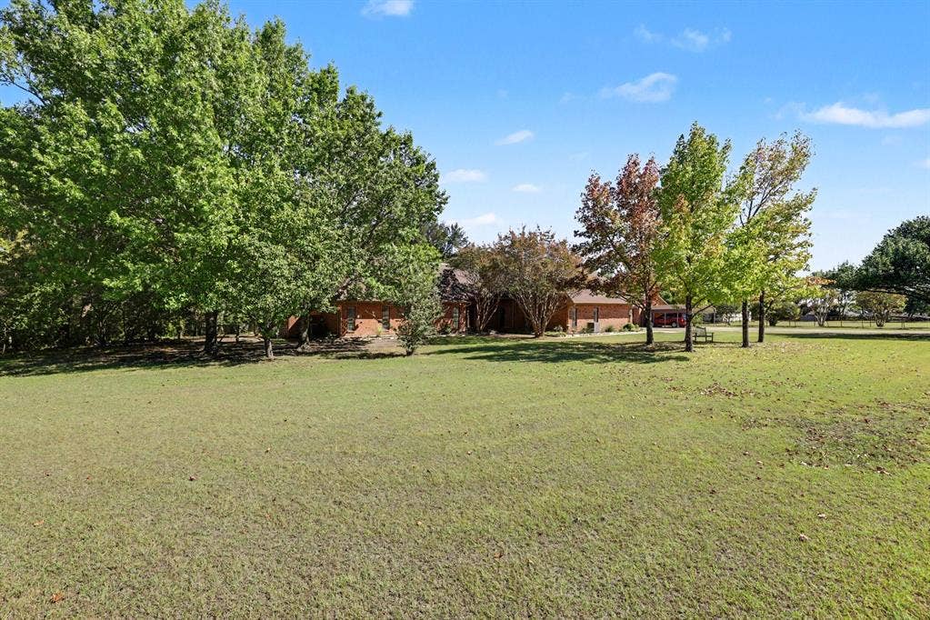 26 Brookhaven Drive, Lucas, TX 75002 Expansive lawn area with mature trees and a brick-clad structure