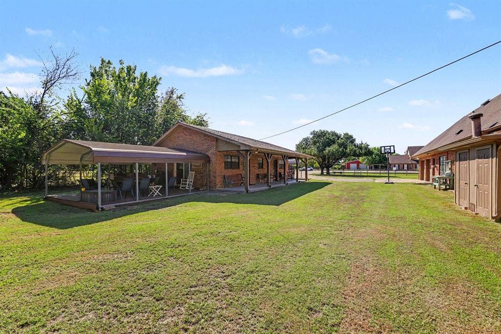26 Brookhaven Drive, Lucas, TX 75002 Expansive grassy yard area with a large covered patio featuring a metal frame and roof, brick exterior, and a secondary structure with exterior doors