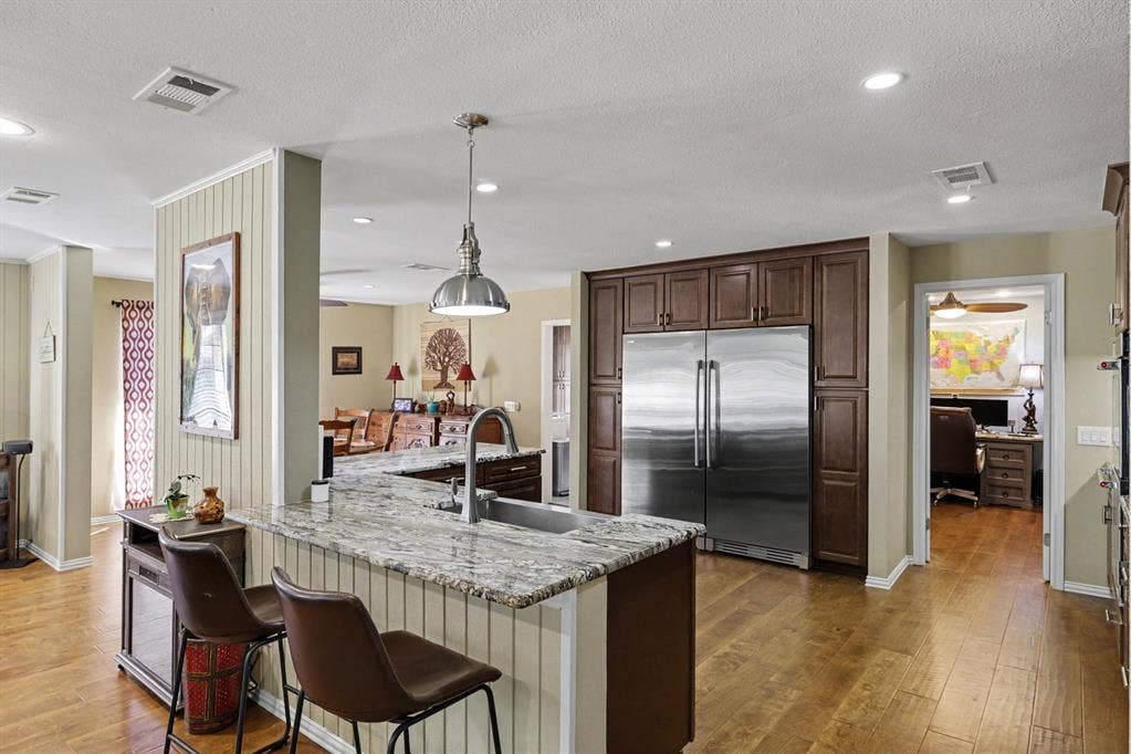 26 Brookhaven Drive, Lucas, TX 75002 Kitchen featuring wood-finish flooring, a granite-top island with beadboard detailing, dark wood cabinetry, and stainless steel appliances