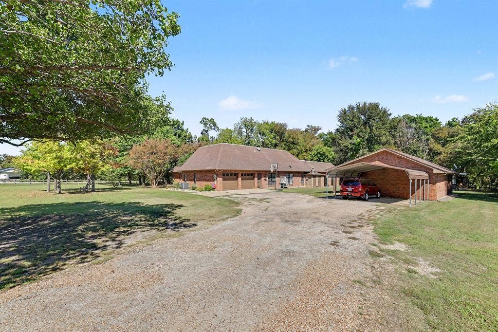 26 Brookhaven Drive, Lucas, TX 75002 Brick exterior residence featuring a two-car garage, expansive gravel driveway, and a detached carport