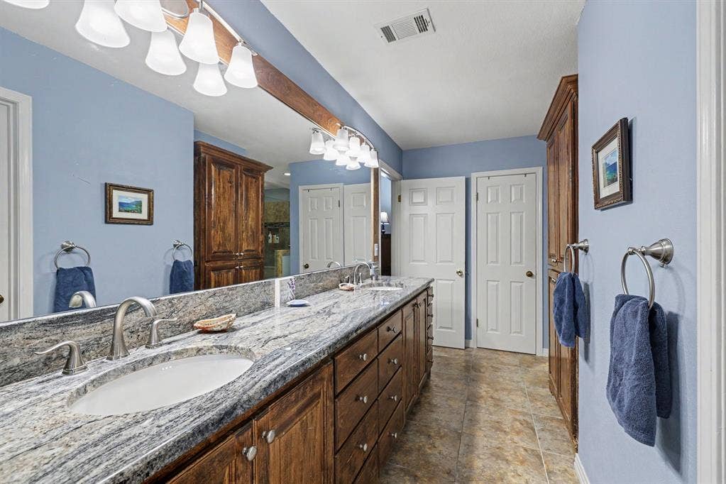 26 Brookhaven Drive, Lucas, TX 75002 Double vanity with undermount sinks, stone countertop, brushed nickel fixtures, custom wood cabinetry, and a full-width mirror