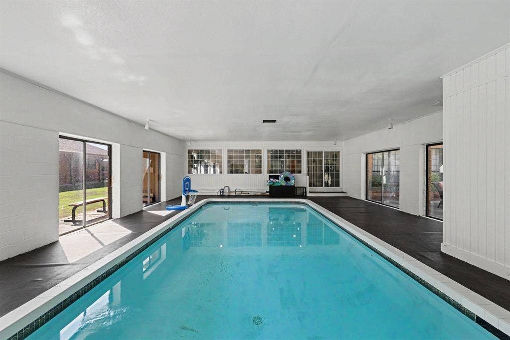 26 Brookhaven Drive, Lucas, TX 75002 Indoor swimming pool with perimeter tiling, multiple large glass sliding doors, transom windows, and white vertical paneling