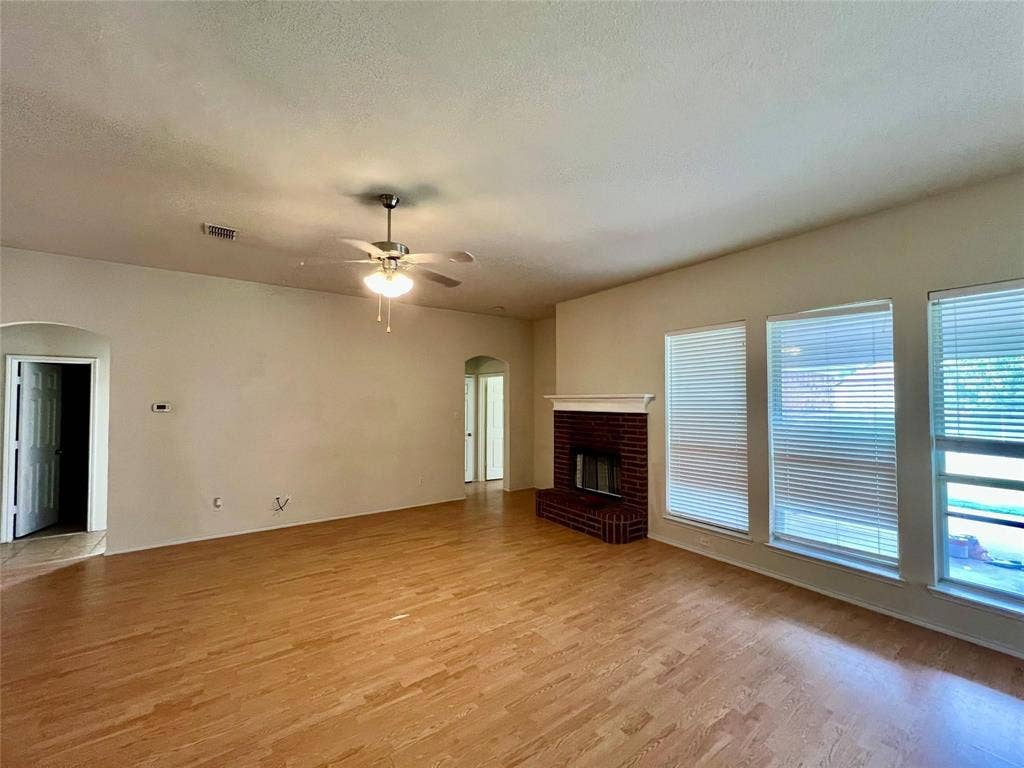 1801 Kathryn Court, Arlington, TX 76018 Spacious room featuring wood-finish flooring, a ceiling fan with integrated lighting, a brick fireplace with a white mantel, and multiple windows