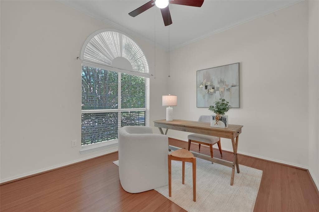 Arched window with blinds, wood-finish flooring, ceiling fan, and crown molding